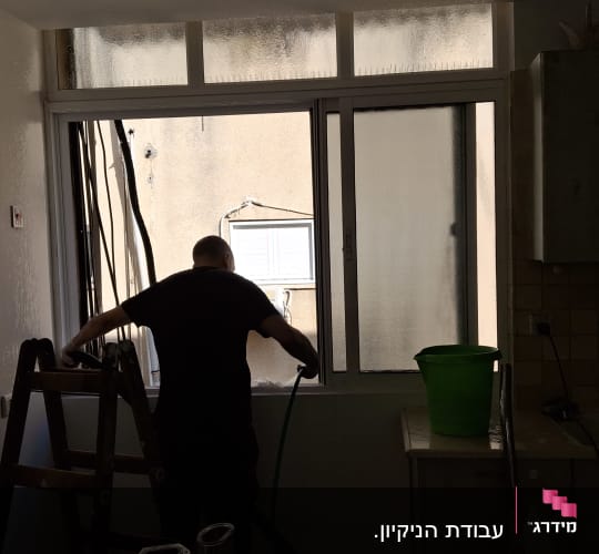 אדם מנקה חלון עם דלי ירוק וסולם